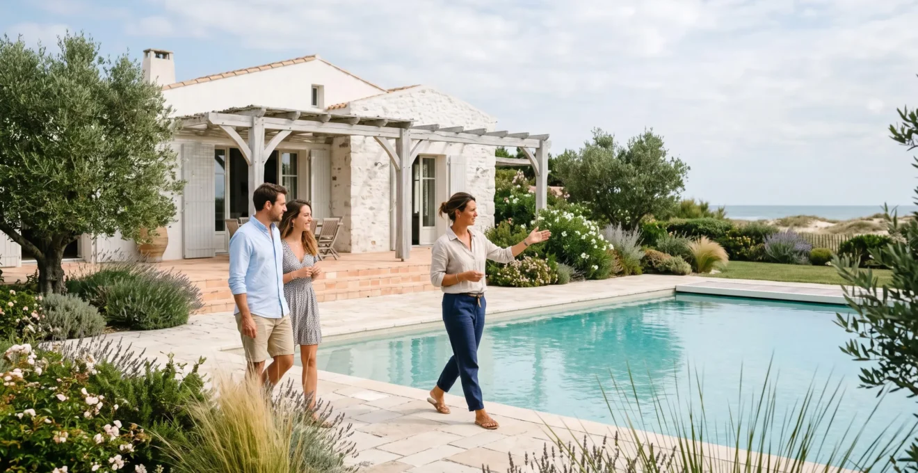 Un hôte accompagne deux visiteurs le long de la piscine d'une villa de vacances au jardin paysager sur le littoral.